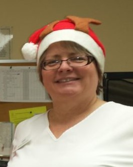 image of Lori proud and smiling in a white scrub top with reindeer santa hat